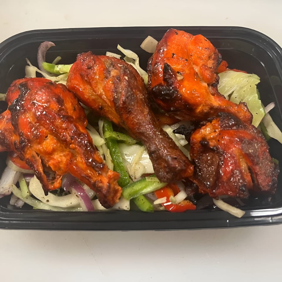 Four pieces of Tandoori chicken drumsticks with charred skin, served over a bed of sliced vegetables.