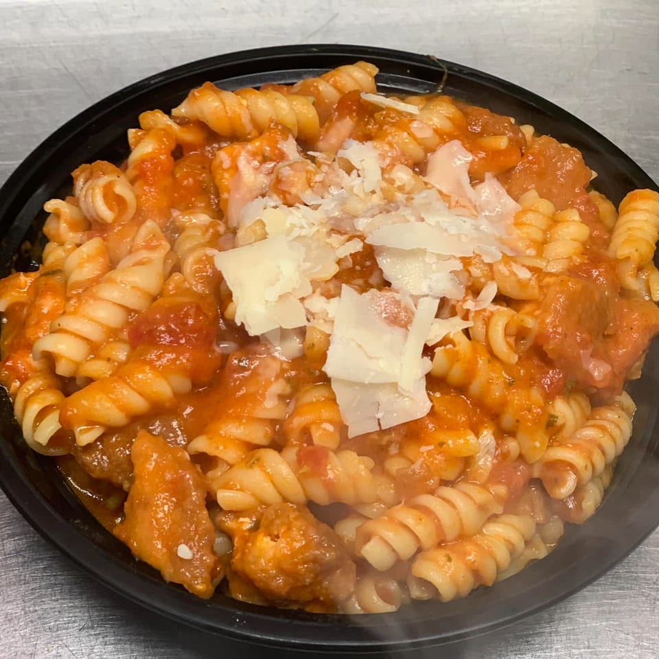Rotini pasta with red sauce, chicken, and shaved parmesan cheese in a black bowl.