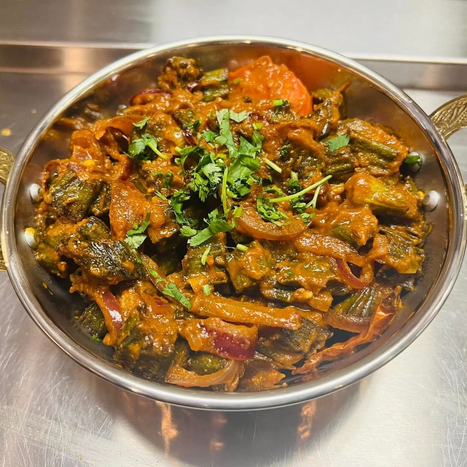 A close-up of a vibrant Indian okra curry, garnished with fresh cilantro, in a metal bowl.