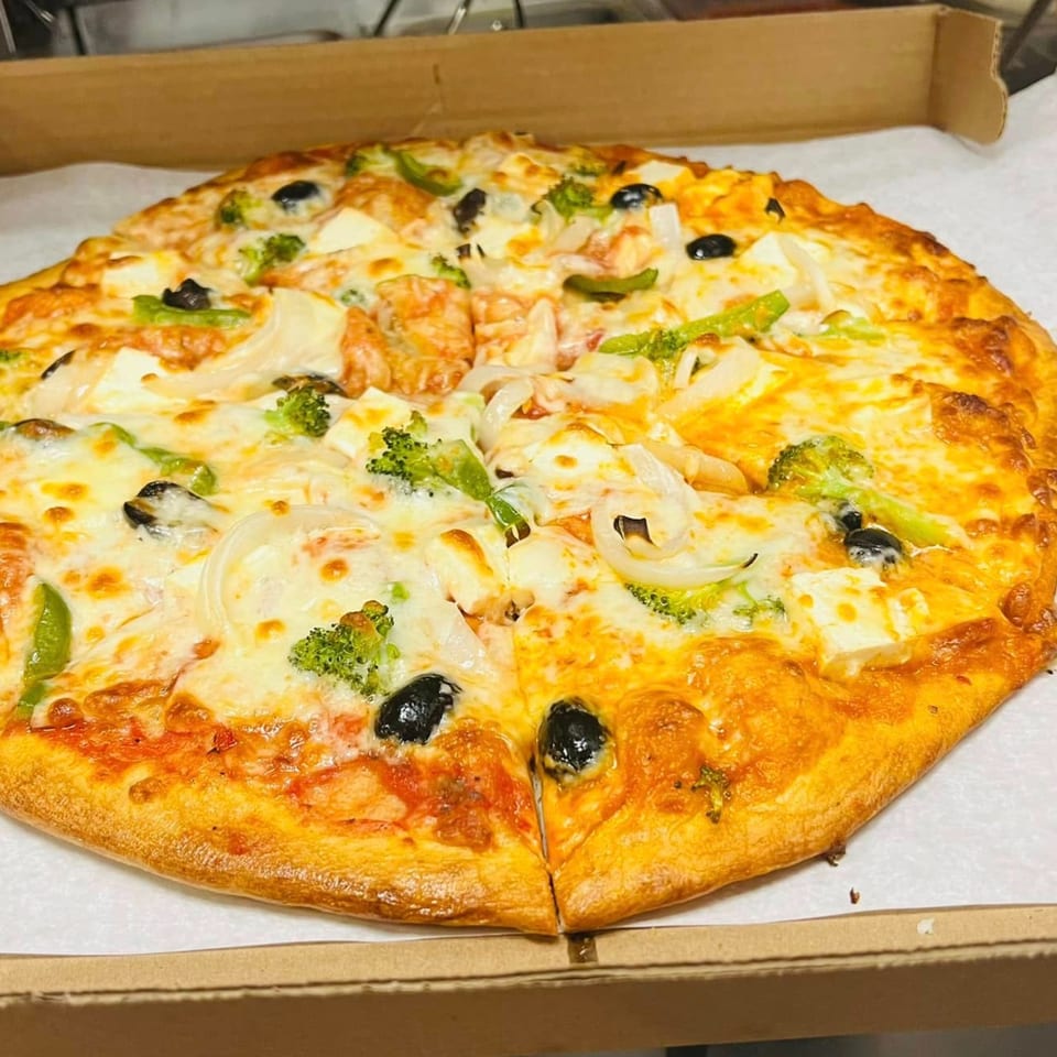 A whole pizza with melted cheese, broccoli, onions, black olives, and green peppers in a box.