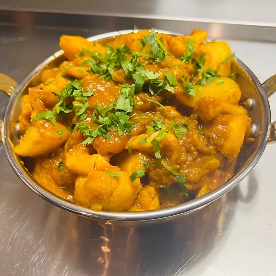 Aloo Gobi, an Indian dish with potatoes and cauliflower in a rich, orange sauce, garnished with cilantro.