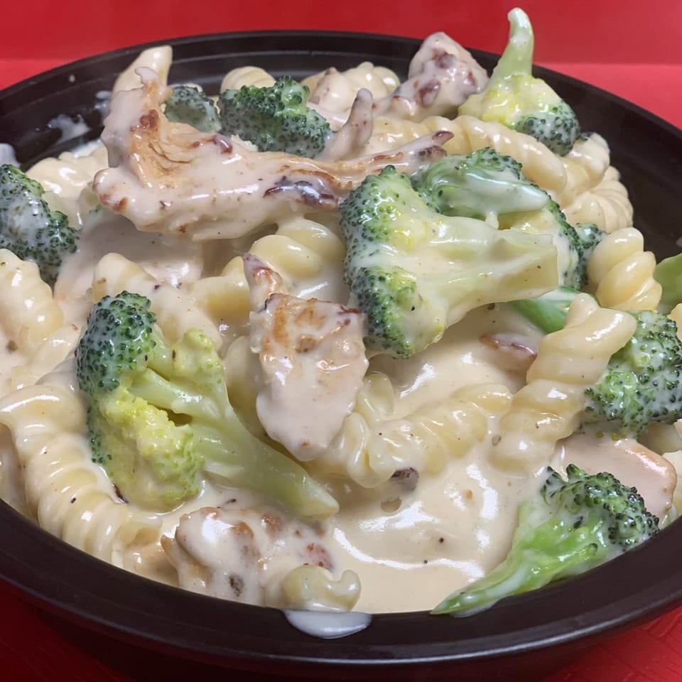 Creamy pasta with chicken and broccoli florets in a dark bowl against a red background.