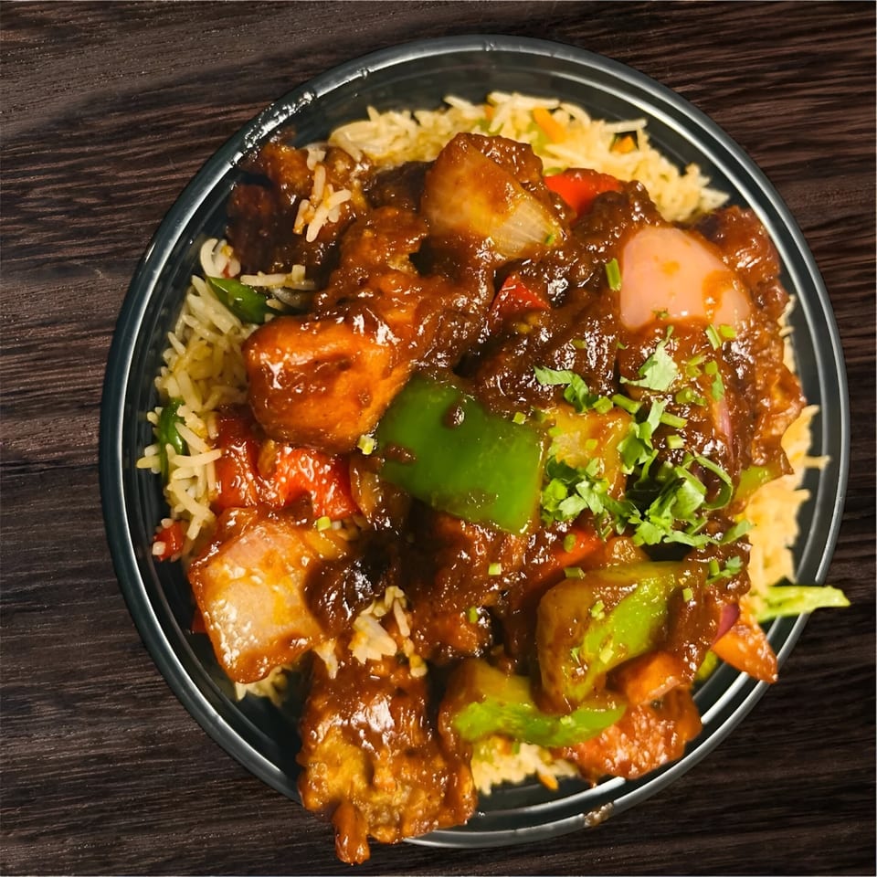 Indian chili chicken with bell peppers and onions, served over rice in a black bowl.