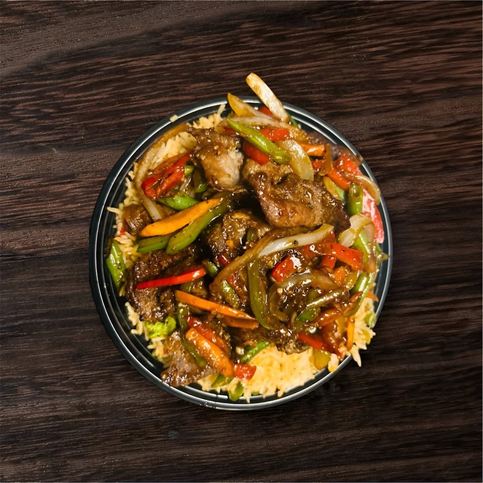 Indian stir-fried beef with colorful vegetables and rice in a black bowl on a dark wooden table.